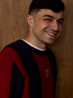 Model masculí somrient amb un jersei de ratlles negres i vermelles de FC Barcelona amb l'escut del club al pit.