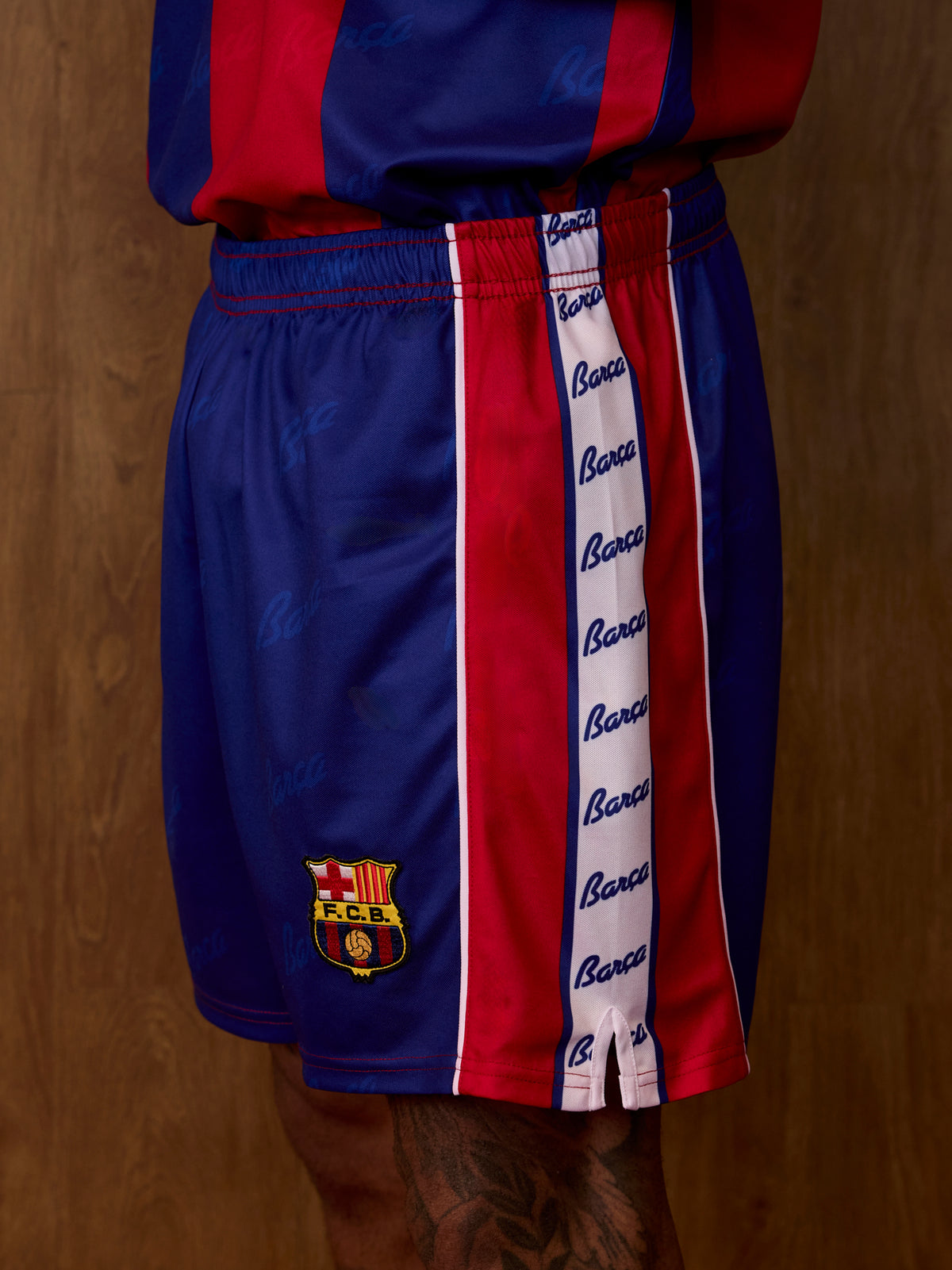 Vue latérale du short FC Barcelona en bleu et rouge, avec une bande verticale script Barça et l’écusson du club sur la jambe.