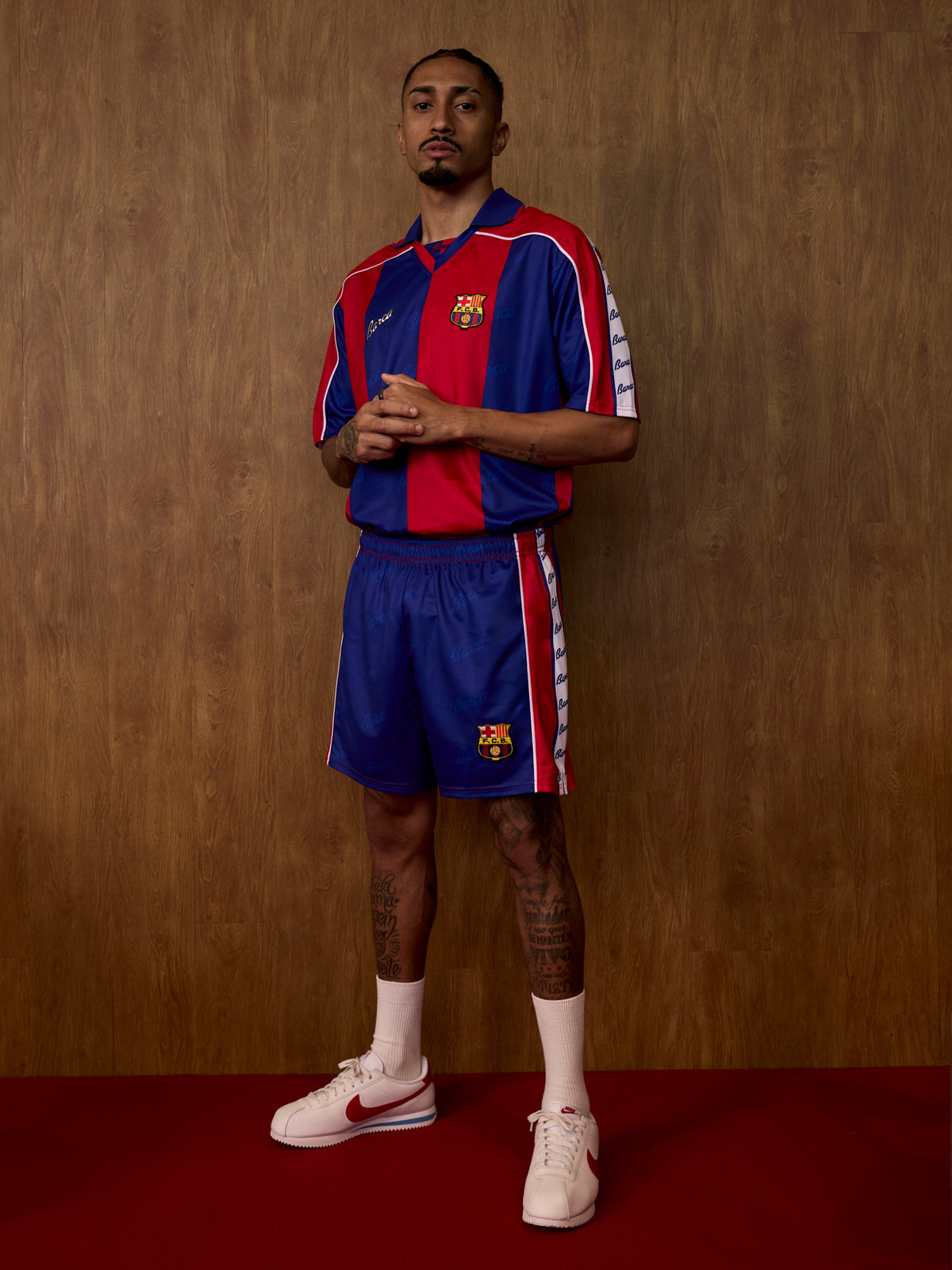 Model amb una equipació retro del FC Barcelona amb franges verticals blau i grana, pantalons curts a joc, mitjons blancs i sabatilles Nike blanques.
