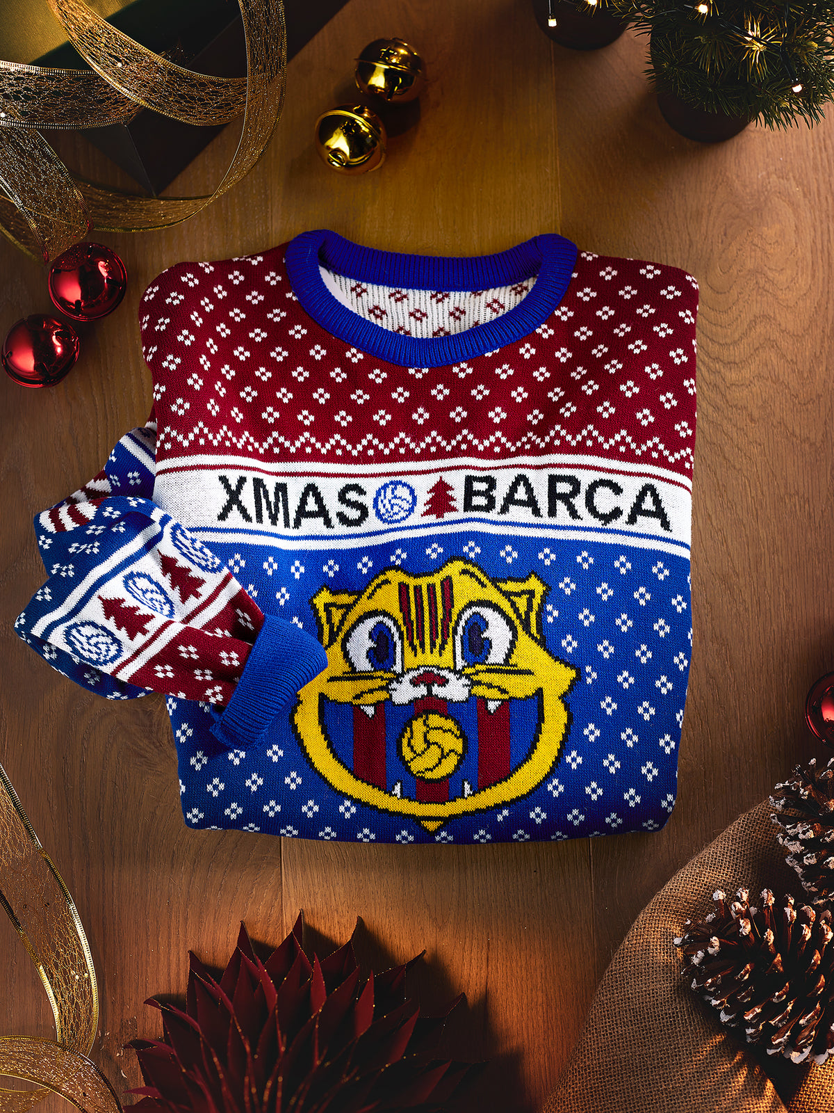 Jersey navideño plegado de FC Barcelona con estampado de copos de nieve en rojo, azul y blanco, cuello de canalé azul y gran escudo del Barça en el frente.