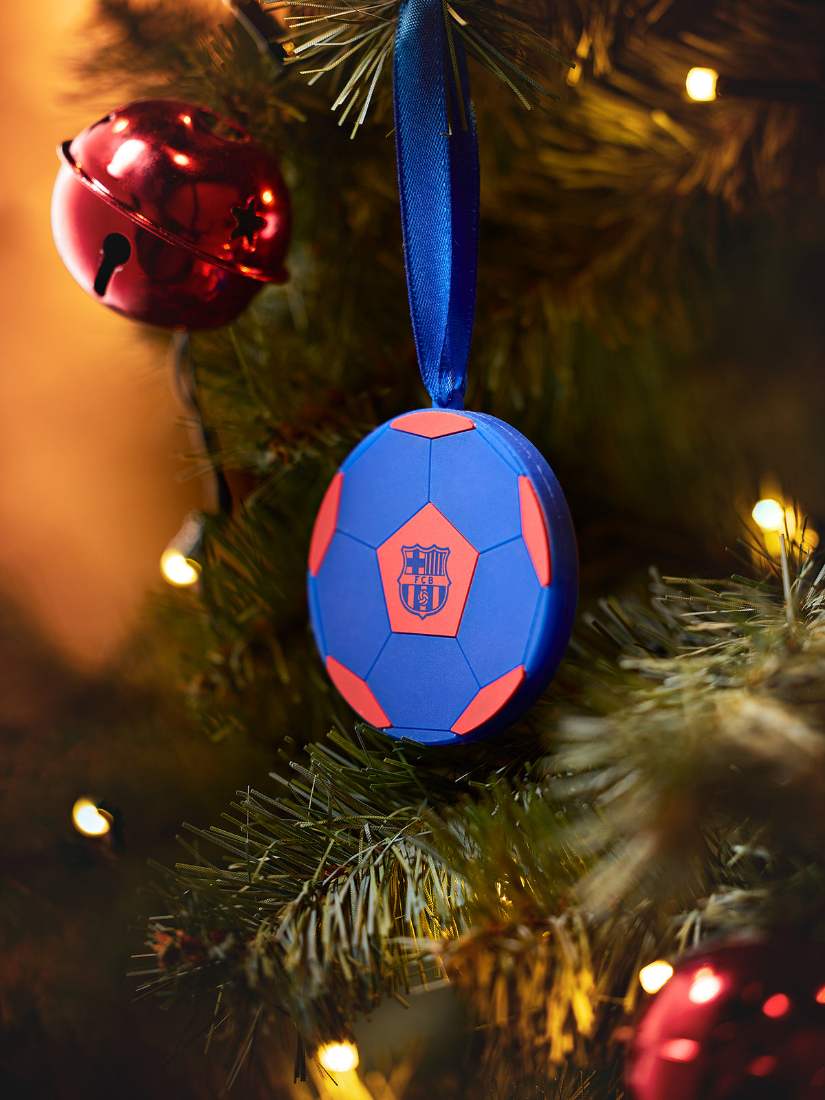 FC Barcelona soccer ball ornament hanging on a Christmas tree with a blue ribbon and coral accents.
