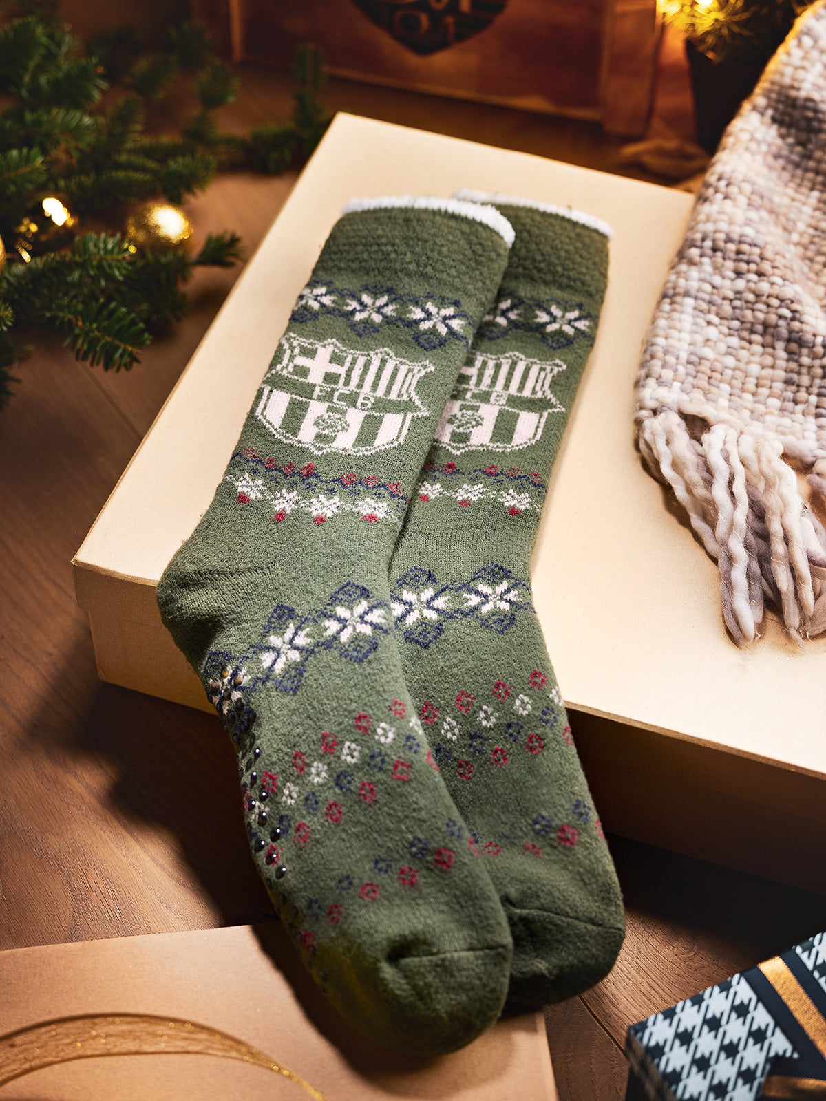 Par de calcetines verdes de FC Barcelona con escudo de Barça tejido y motivos geométricos de estilo invernal, presentados doblados sobre una caja.