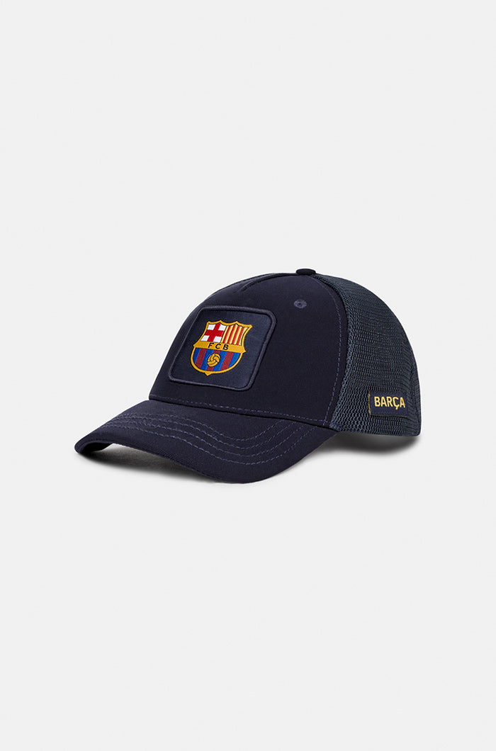 Navy blue FC Barcelona trucker cap with mesh back, embroidered club crest patch on the front panel, and the word “BARÇA” in yellow on the side.


