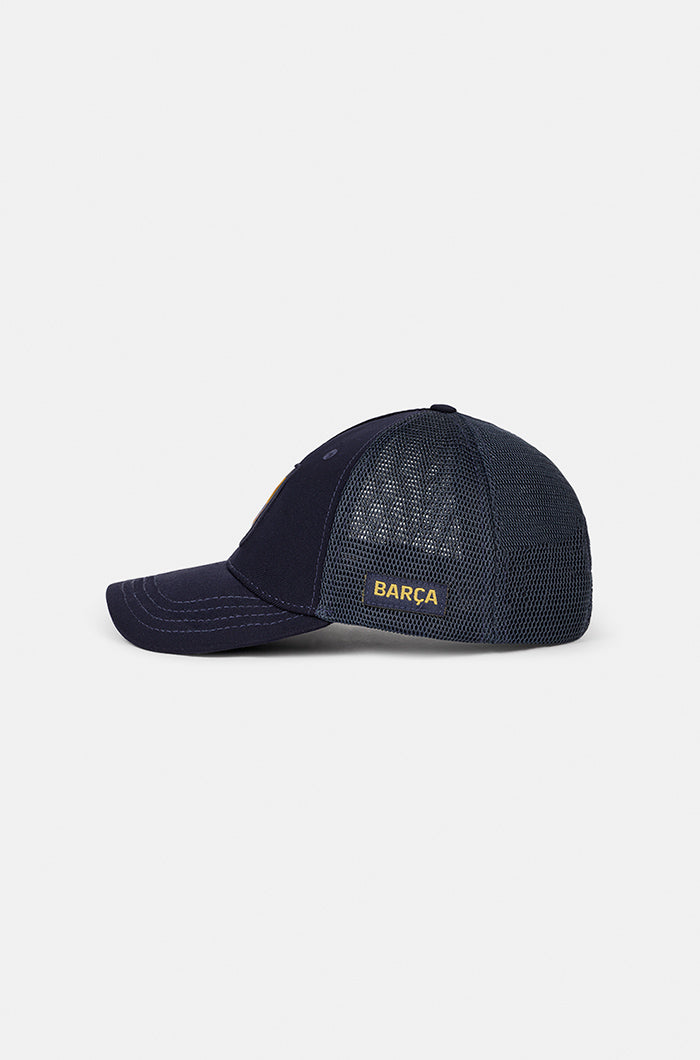 Navy blue FC Barcelona trucker cap with mesh back, embroidered club crest patch on the front panel, and the word “BARÇA” in yellow on the side.