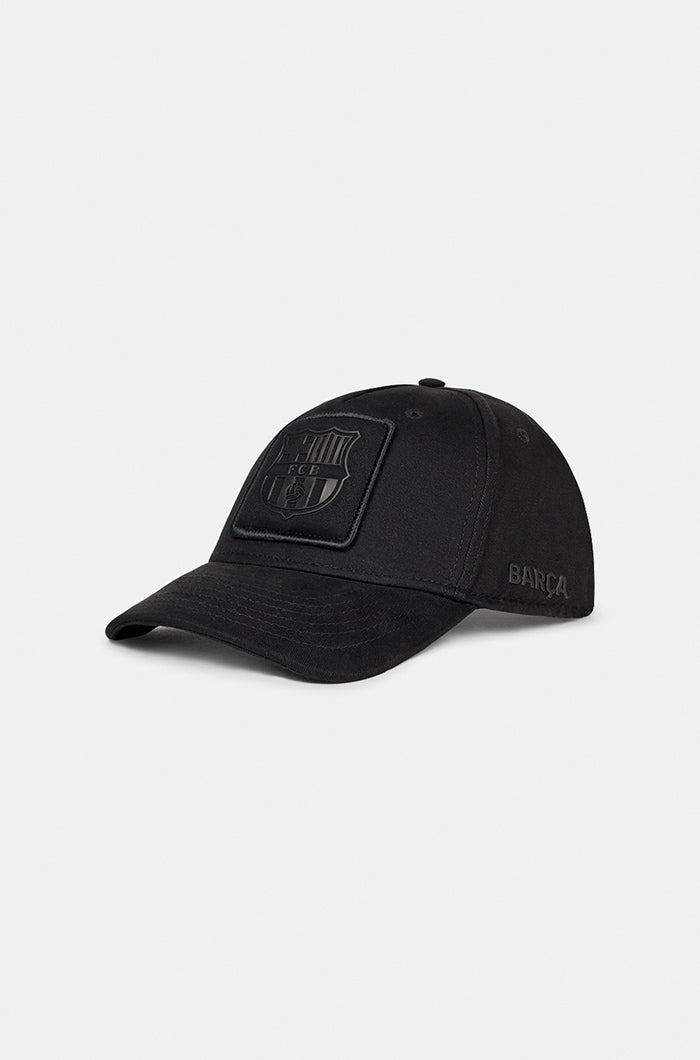 Black FC Barcelona baseball cap with a matte black crest patch on the front and the word "BARÇA" embroidered on the side, featuring a curved brim and structured fit.