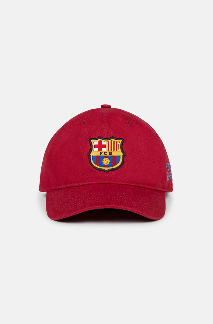Red FC Barcelona baseball cap featuring the club crest on the front and the phrase “FORÇA BARÇA” embroidered in blue on the side.