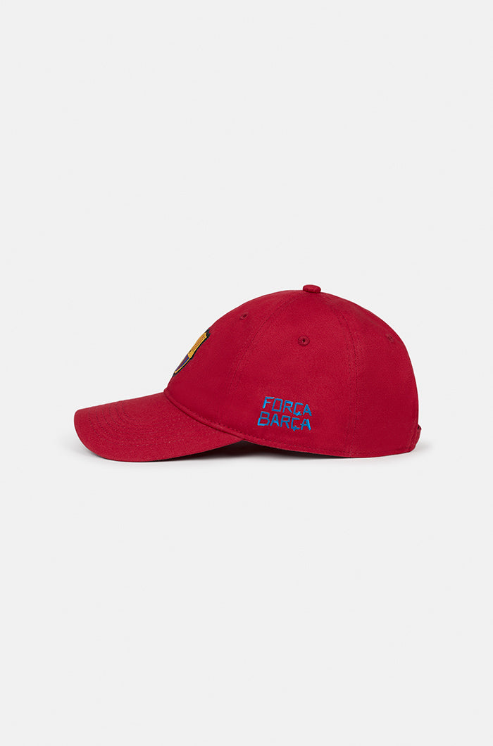 Red FC Barcelona baseball cap featuring the club crest on the front and the phrase “FORÇA BARÇA” embroidered in blue on the side.